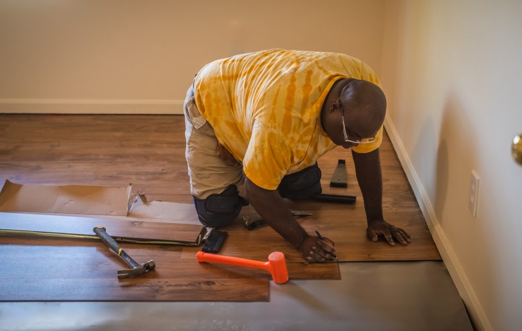 African American carpenter in yellow t-shirt installing new laminated floor